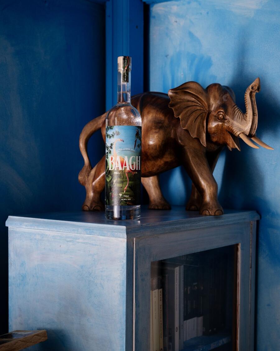 A bottle of Baagh Indian Craft Gin on a blue side table beside a carved wooden elephant